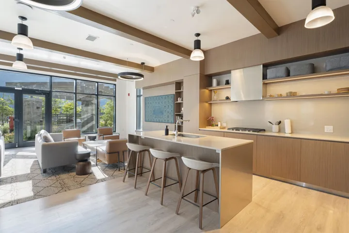 Open-concept space featuring a kitchen with light wood-finish cabinetry, a large center island with seating, a built-in range, and a sleek range hood