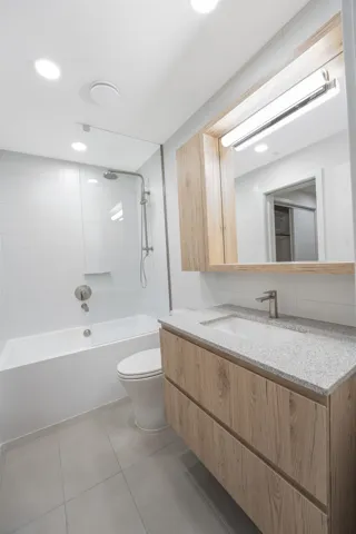 Modern bathroom featuring a wood-finish vanity with a light speckled countertop and undermount sink