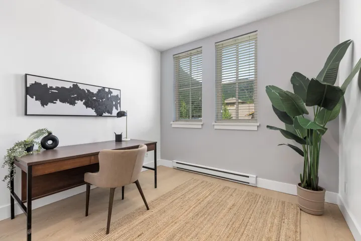 Dedicated room featuring two windows with blinds, light wood-finish flooring, and a baseboard heating unit