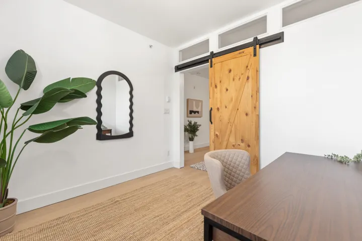 White interior with barn door featuring natural wood finish and black hardware, complemented by white baseboards and light wood-finish flooring