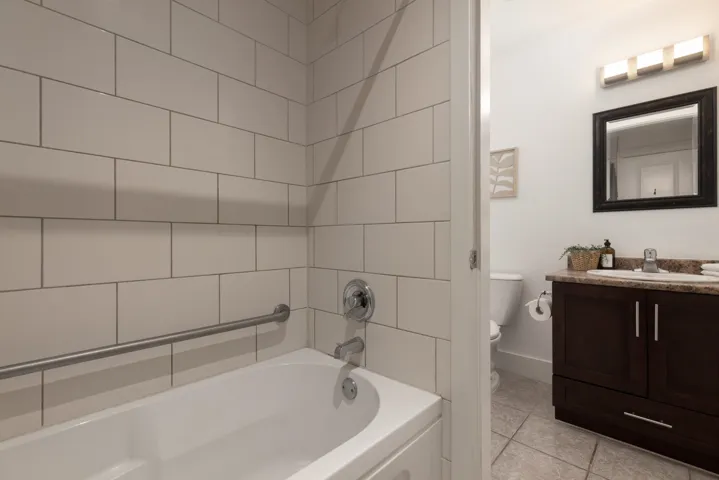 Bathroom featuring a subway-tiled bath surround, built-in grab bar, and a dark wood-finish vanity with a light-toned countertop