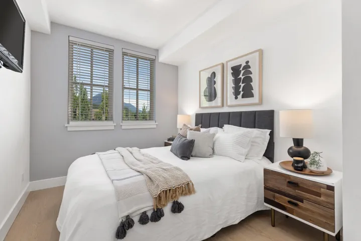Bedroom featuring two windows with horizontal blinds, light wood-finish flooring, a paneled headboard, and recessed lighting