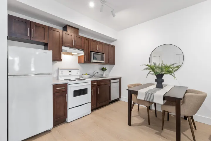Compact kitchen featuring dark wood cabinetry, white appliances, and light-tone wood-finish flooring