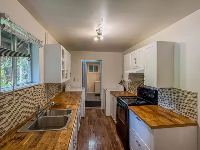 Kitchen with butcher block countertops, electric range, tasteful backsplash, white cabinets, and glass insert cabinets