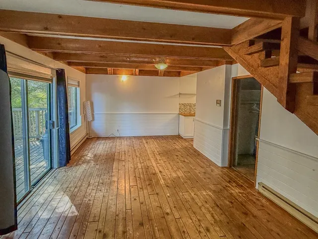 Unfurnished room featuring wainscoting, beam ceiling, hardwood / wood-style flooring, and stairs