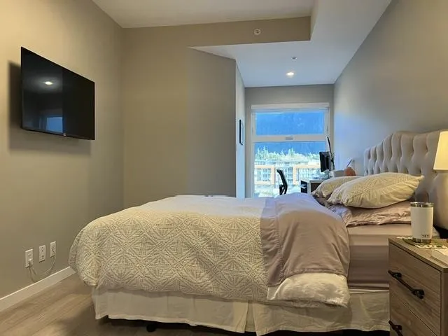 Bedroom featuring a wall-mounted television, wood-finish flooring, recessed lighting, and a large window with a roller blind