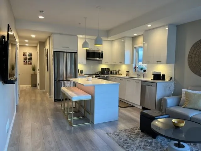 Open concept living area featuring a modern kitchen with sleek white cabinetry, stainless steel appliances, a white tile backsplash, and light wood-finish flooring throughout