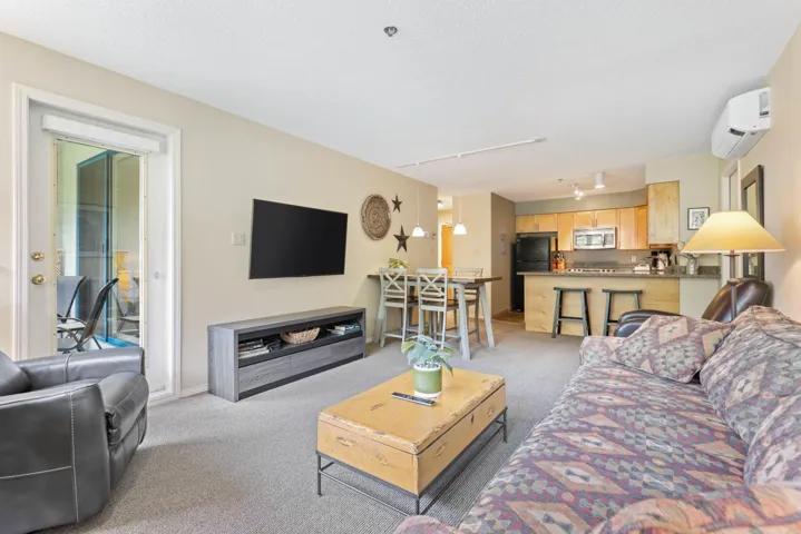 Living area featuring a wall unit AC, light carpet, track lighting, and baseboards