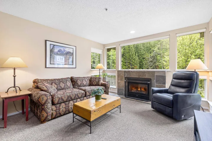 Carpeted living area featuring a textured ceiling, healthy amount of natural light, and a glass covered fireplace