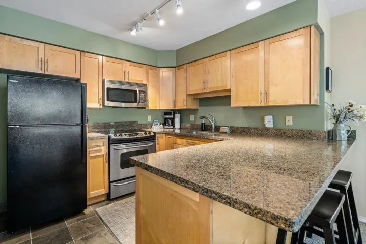 Kitchen with appliances with stainless steel finishes, a sink, light brown cabinets, a peninsula, and a breakfast bar