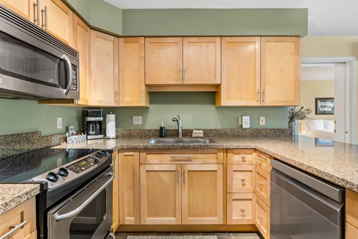 Kitchen with stainless steel appliances, a sink, light brown cabinets, and stone counters