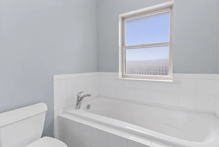 Integrated bathtub with chrome fixtures, surrounded by white square wall tiles and a decorative trim