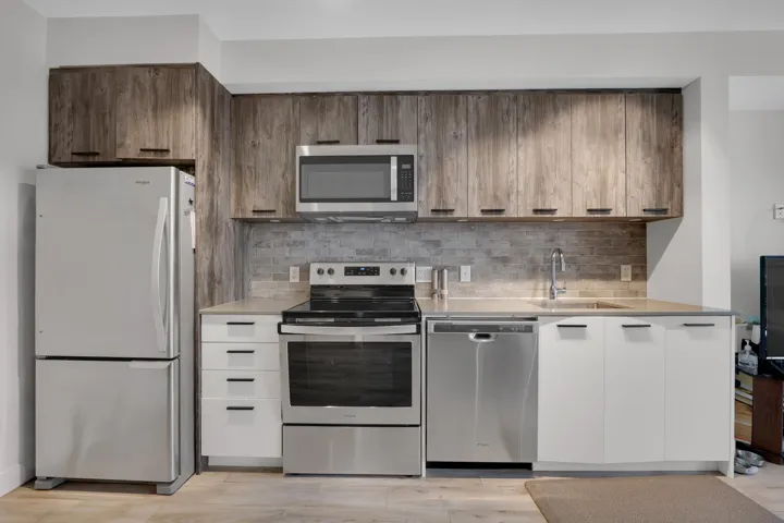 Kitchen featuring stainless steel appliances, backsplash, light wood finished floors, and light stone counters