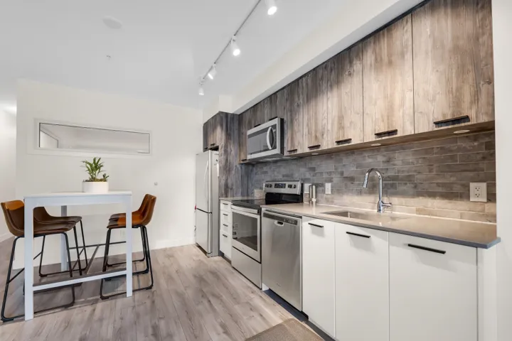 Kitchen featuring stainless steel appliances, light wood-style floors, modern cabinets, tasteful backsplash, and light stone countertops