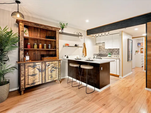 Kitchen with under cabinet range hood, white cabinetry, light countertops, light wood-style flooring, and tasteful backsplash