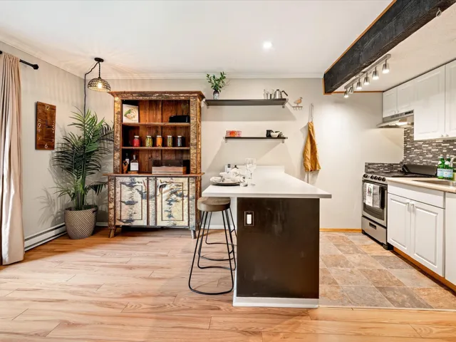 Kitchen with stainless steel gas range oven, crown molding, baseboard heating, under cabinet range hood, and white cabinetry