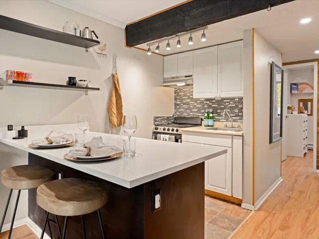 Kitchen featuring stainless steel range, under cabinet range hood, white cabinetry, a kitchen bar, and open shelves