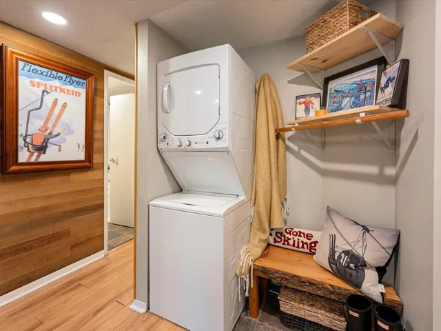 Laundry area featuring stacked washer / dryer, light wood finished floors, wooden walls, and recessed lighting