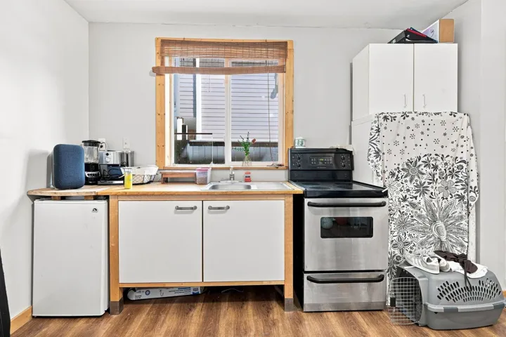 Compact kitchen area featuring wood-finish flooring, light wood-tone countertops, and white cabinetry