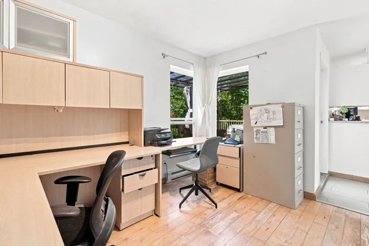 Dedicated workspace featuring wood-finish flooring, light wood built-in desk cabinetry, and two windows providing abundant natural light