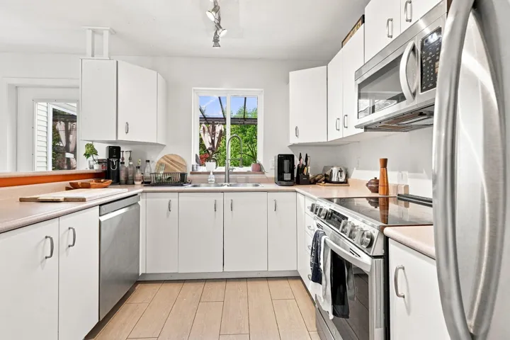 Kitchen featuring white cabinetry, stainless steel appliances, wood-finish flooring, a window above the sink, and track lighting
