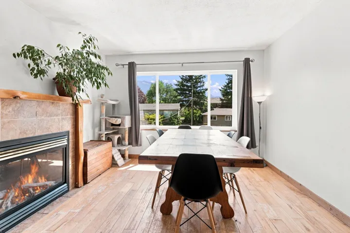 Dining space featuring a stone-clad fireplace with a wood mantle, wood-finish flooring, and a large window