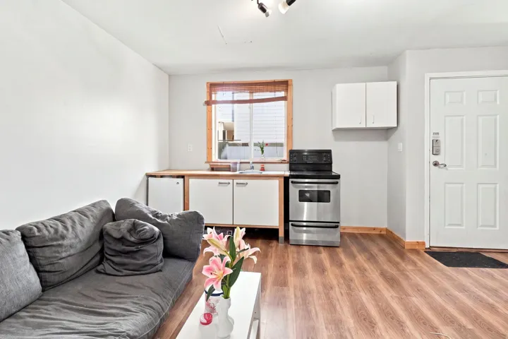 Open-concept space featuring wood-finish flooring, a kitchen area with stainless steel appliances, and a white paneled entry door