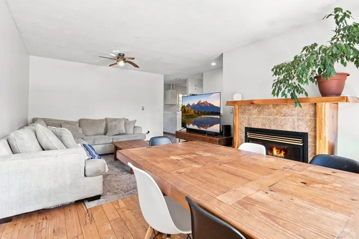 Living area featuring a fireplace with a tile surround and wood mantel, wood-finish flooring, and a ceiling fan