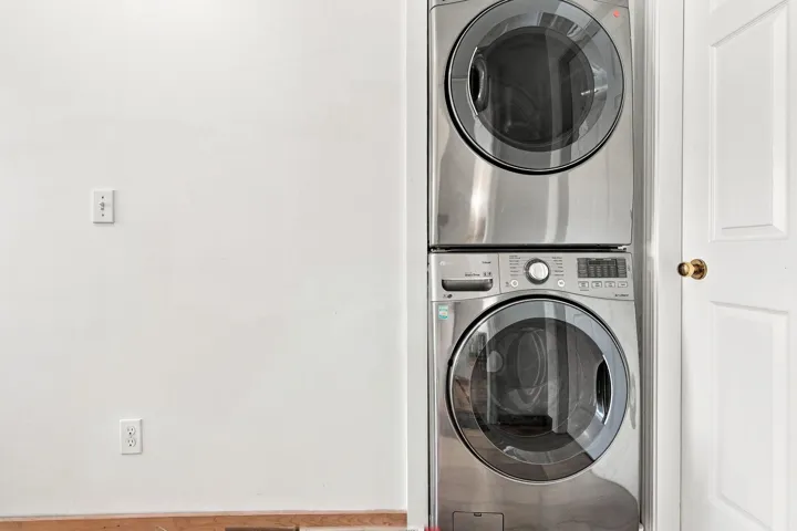 Laundry area featuring a stacked washer and dryer unit, white walls, and wood-finish flooring