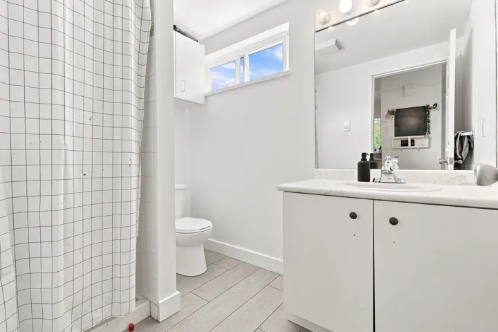 Bathroom featuring a white vanity with integrated sink, a rectangular mirror with strip lighting, window, and wood-finish flooring