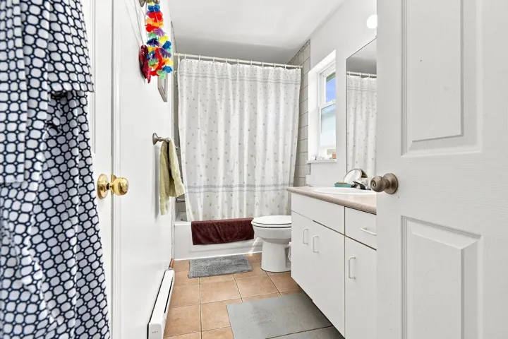 Full bathroom featuring a white vanity with integrated sink, a built-in tub with shower, and tiled flooring