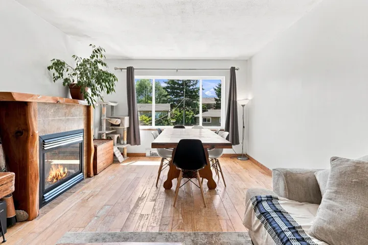 Spacious living area featuring light wood-finish flooring, a prominent fireplace with a wood mantle and tile surround, and expansive windows providing abundant natural light