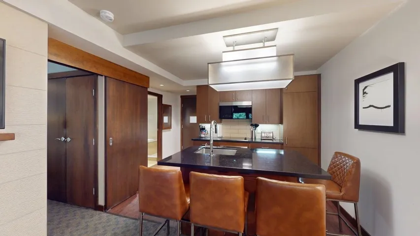 Kitchen with tasteful backsplash, a center island with sink, a kitchen breakfast bar, stainless steel microwave, and dark stone countertops