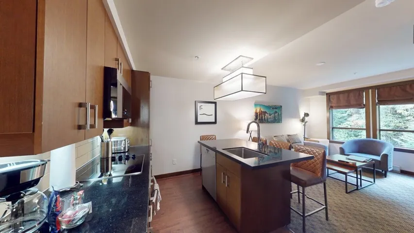 Kitchen with a center island with sink, a kitchen breakfast bar, brown cabinetry, modern cabinets, and dark wood-type flooring