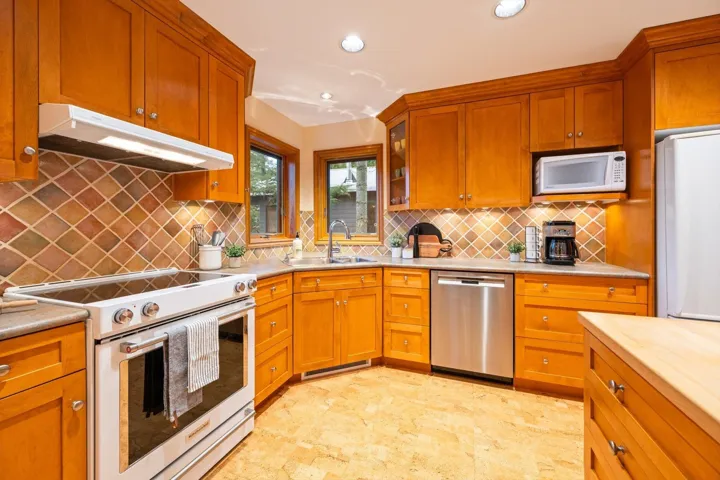 Kitchen with white appliances, wood finish cabinetry, recessed lighting, glass insert cabinets, and light stone countertops
