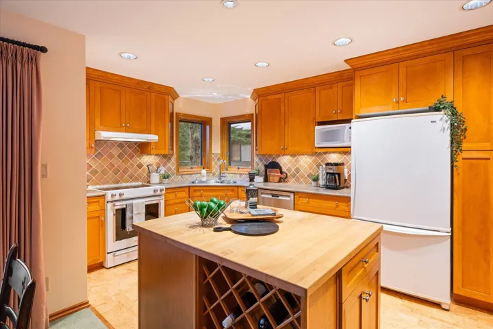 Kitchen with white appliances, butcher block countertops, recessed lighting, wood finish cabinets, and a kitchen island