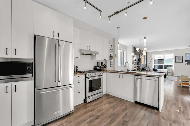 Kitchen with stainless steel appliances, white cabinetry, open floor plan, a peninsula, and light wood-type flooring