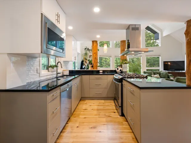 Kitchen featuring appliances with stainless steel finishes, island range hood, light wood finished floors, modern cabinets, and a peninsula