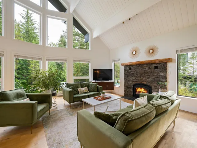Living room featuring beamed ceiling, high vaulted ceiling, a stone fireplace, and light wood finished floors