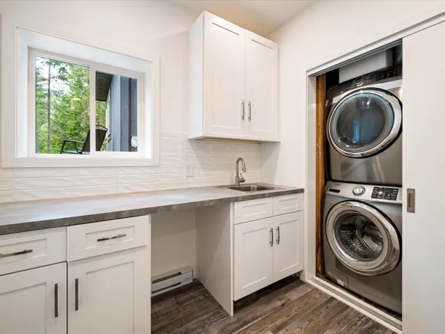 Laundry area with stacked washer / drying machine, dark wood-style flooring, and a baseboard heating unit