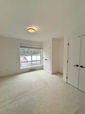 Unfurnished bedroom with a baseboard heating unit, carpet flooring, baseboards, and multiple closets