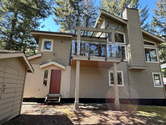 Multi-level exterior featuring vertical siding, shingle siding, a red entry door, a second-story deck with glass railings, and a prominent chimney