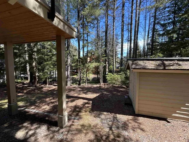 Wood-paneled deck with glass railing, supported by sturdy columns, overlooking a natural, wooded landscape