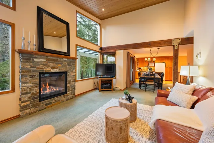 Vaulted wood-paneled ceiling, stone-faced fireplace, large picture windows, wood beam accents, and wood-finish flooring