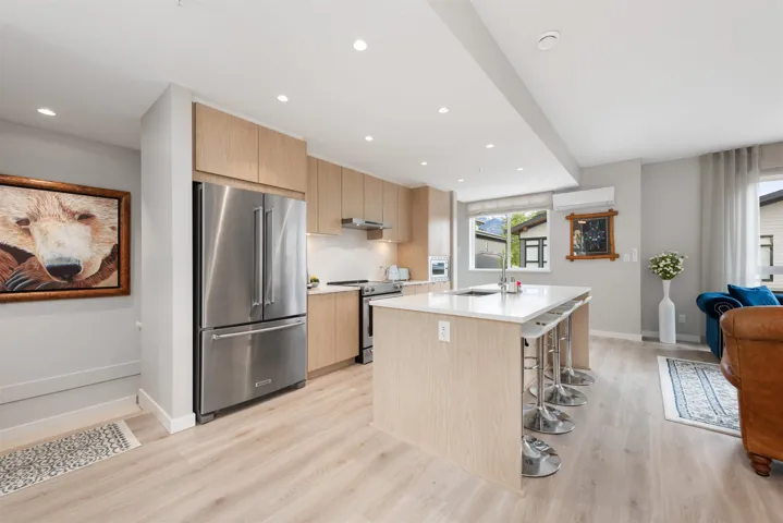 Kitchen featuring stainless steel appliances, light wood-style floors, under cabinet range hood, light countertops, and a kitchen island with sink