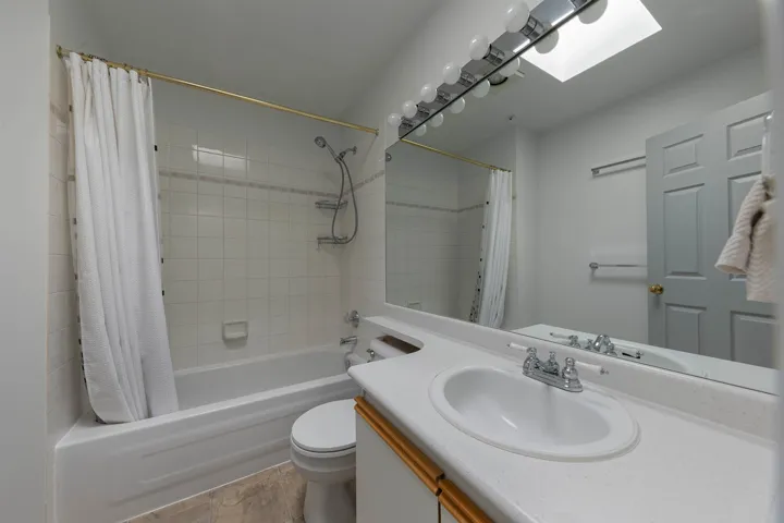 Full bath featuring vanity, shower / bathtub combination with curtain, and a skylight