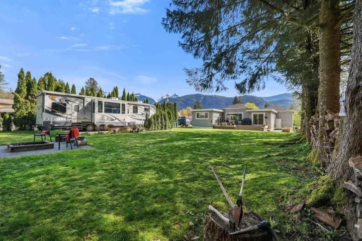 Expansive grassy yard with mature trees, a designated fire pit area, and a residential structure featuring multiple glass doors opening onto a wood-finish deck