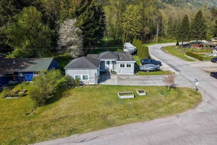 Light grey siding residence featuring a dark shingle roof, paved driveway, and a front lawn with two raised garden beds