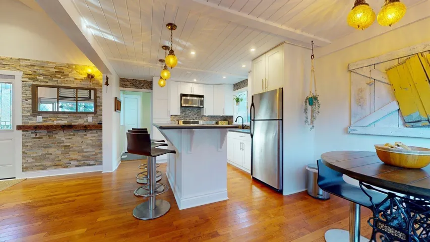 Kitchen with a kitchen bar, white cabinetry, stainless steel appliances, light wood-style flooring, and dark countertops