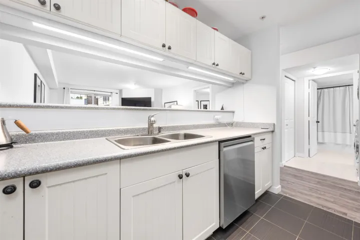 Kitchen featuring dark tile patterned flooring, stainless steel dishwasher, a sink, and white cabinets